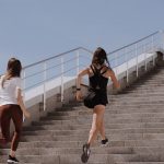 Two women running up stairs outdoors, embodying fitness and wellness.